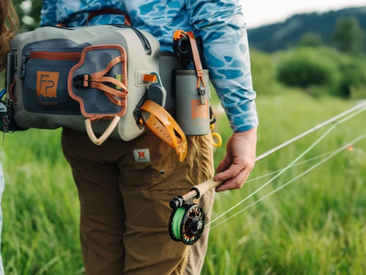 an angler holds a fly fishing rod while walking