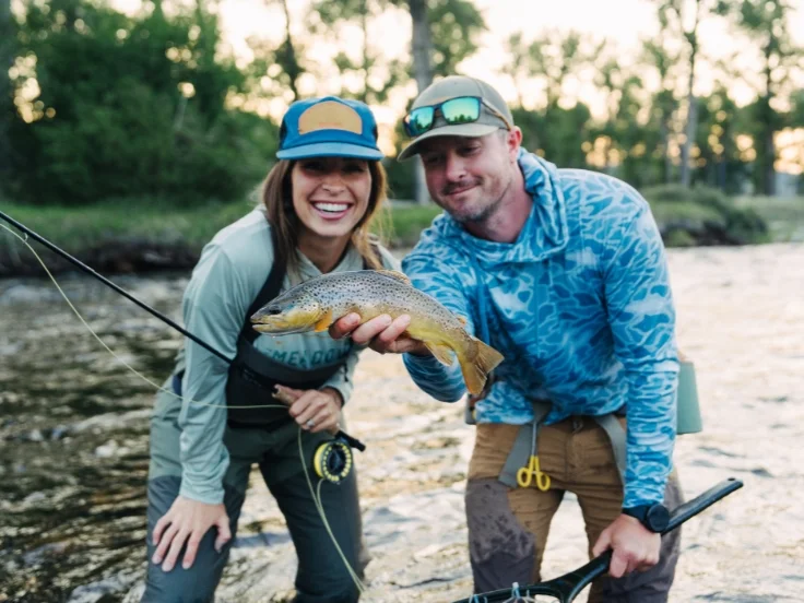 two anglers hold a brown trout while fly fishing on a river