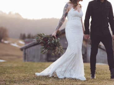 a bride and groom walk across green grass while holding a large bouquet