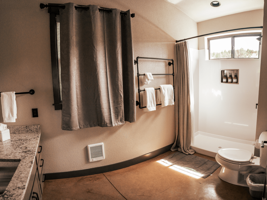 a bathroom with white walls and a large curtain covering a window. The shower curtain is pushed to the side revealing the large shower.
