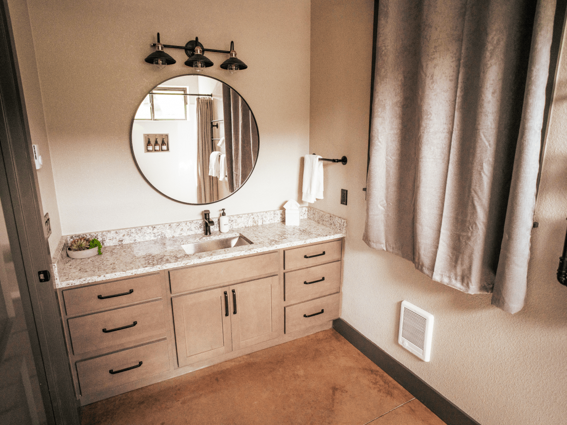 part of a bathroom in a cabin. The countertop is white granite and their is a large round mirror above it.
