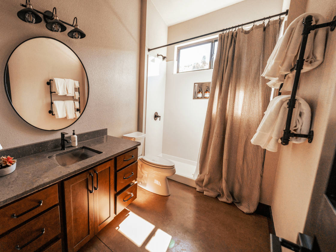 a bathroom with a half drawn shower curtain, natural light coming in through a high window