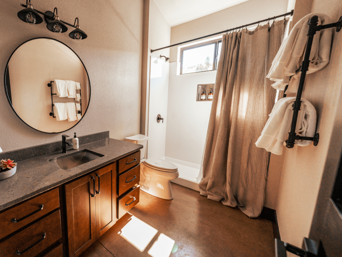 the bathroom of a luxury cabin rental featuring granite countertops, a large mirror, and a large shower with the shower curtain pulled halfway across.