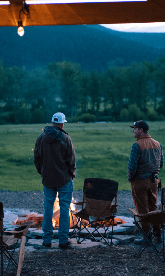 two men stand at a campfire overlooking upper Rock Creek, Montana