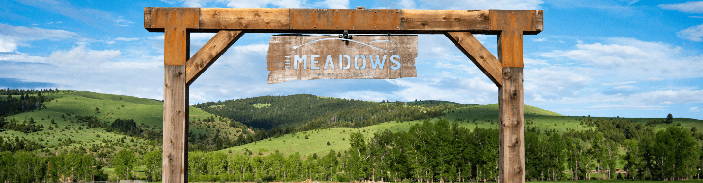 The front entrance sign at The Meadows on Rock Creek. The sky is blue and the hills are a luscious green in the background.