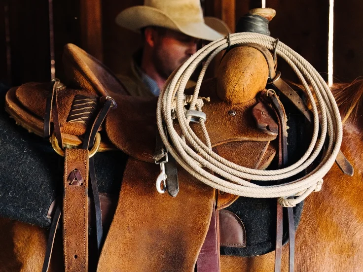 a man saddles up a horse in a barn