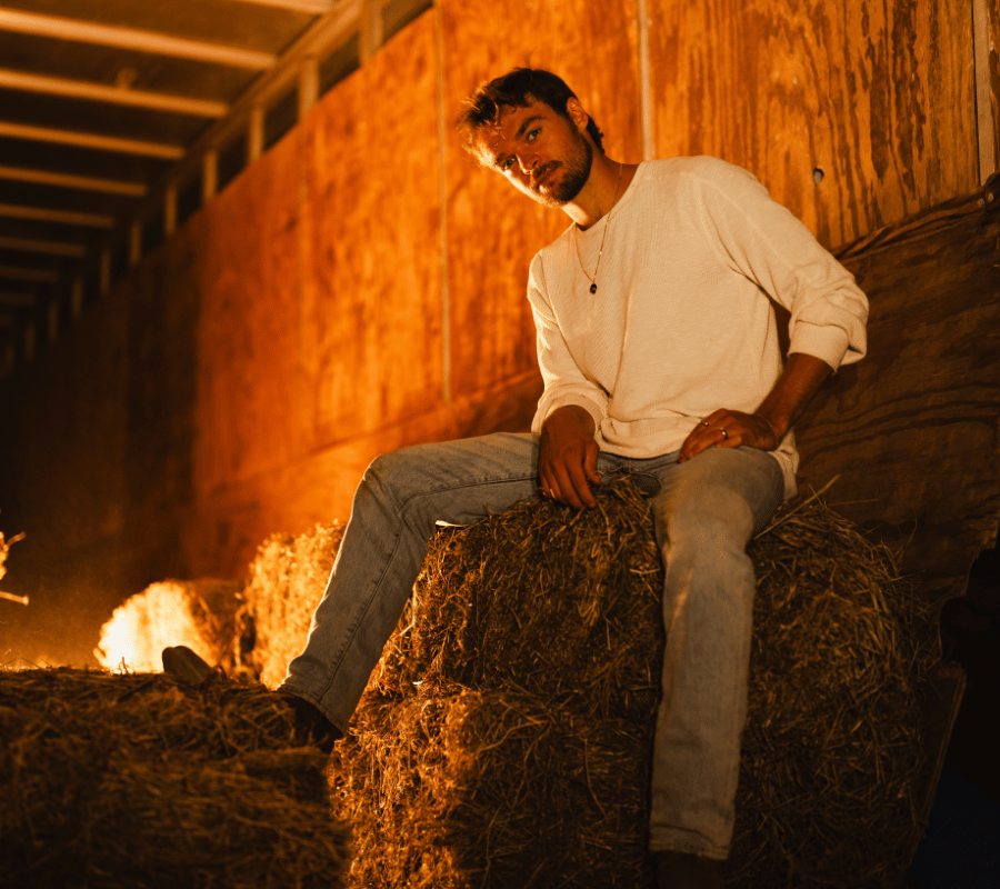 man in white shirt sits on bale of hay