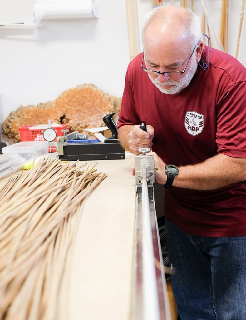 a man planes a piece of split cane bamboo for making a fly fishing rod