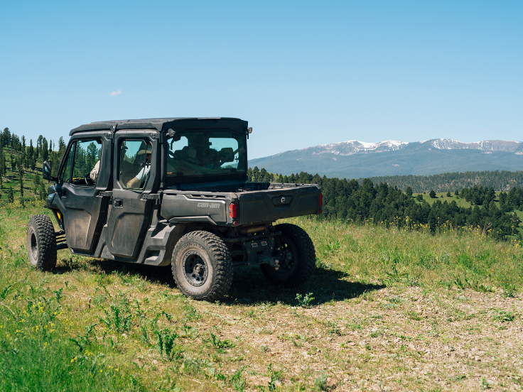 a can am UTV drives on a road with mountains in the background