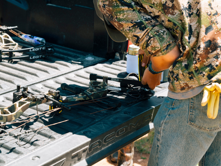 man adjusts a bow and arrow on a tailgate