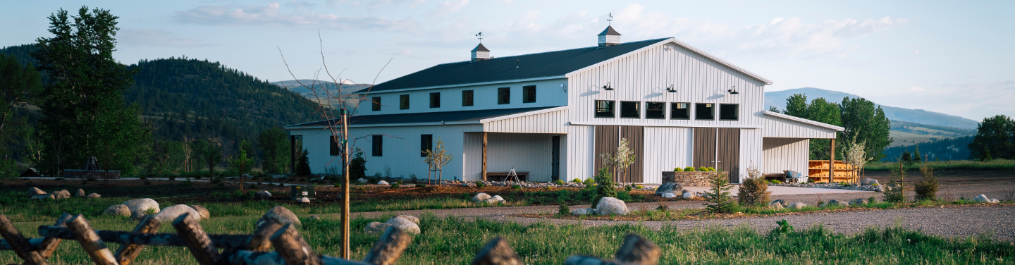 a white barn in a grassy field with a wooden fence near it