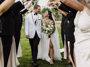 a bride and groom look at each other while walking by their bridal party