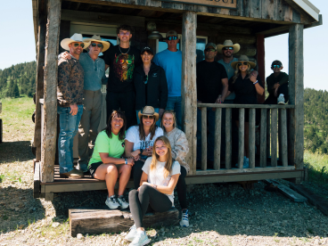 a family stands on the doorstep of a rustic cabin in the mountains