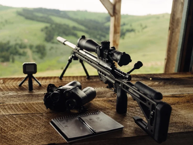 a rifle sits on a table with a long range in the background