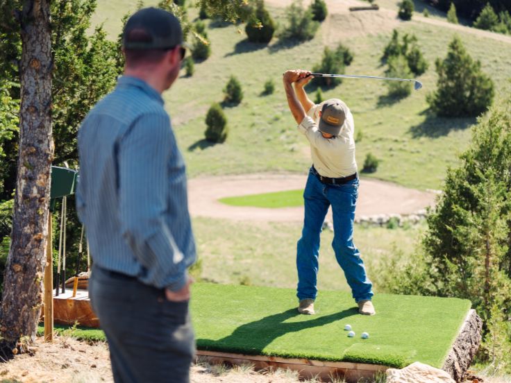 man swings a golf club on a green