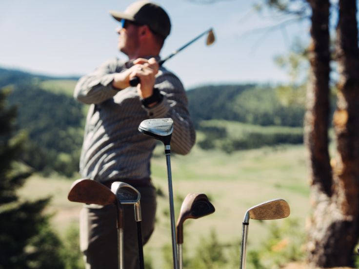 man swings a club at a golf course in the mountains of montana