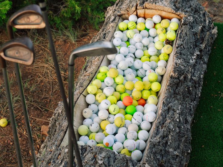 a number of golf balls sitting in a carved out log by some golf clubs
