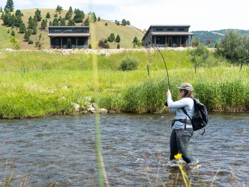 a woman fly fishing in a river in front of two cabins