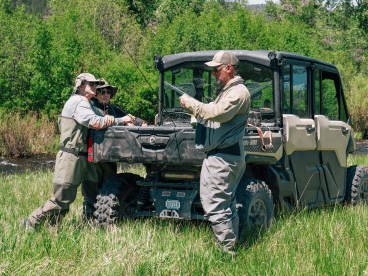 three people standing around a UTV in a grassy field