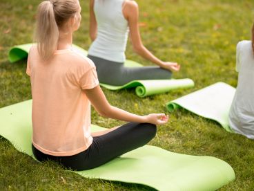 multiple women sitting on green yoga mats in the grass