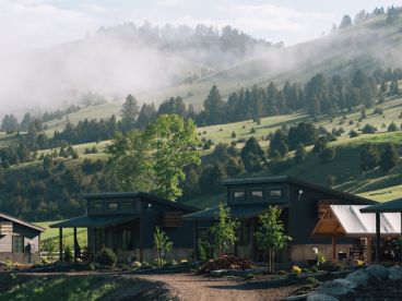 two cabins beneath a green mountain with fog on it