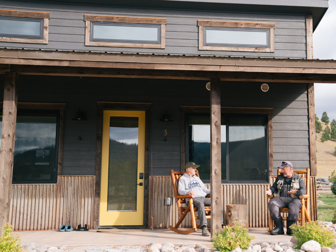 two men sit in rocking chairs in front of a cabin