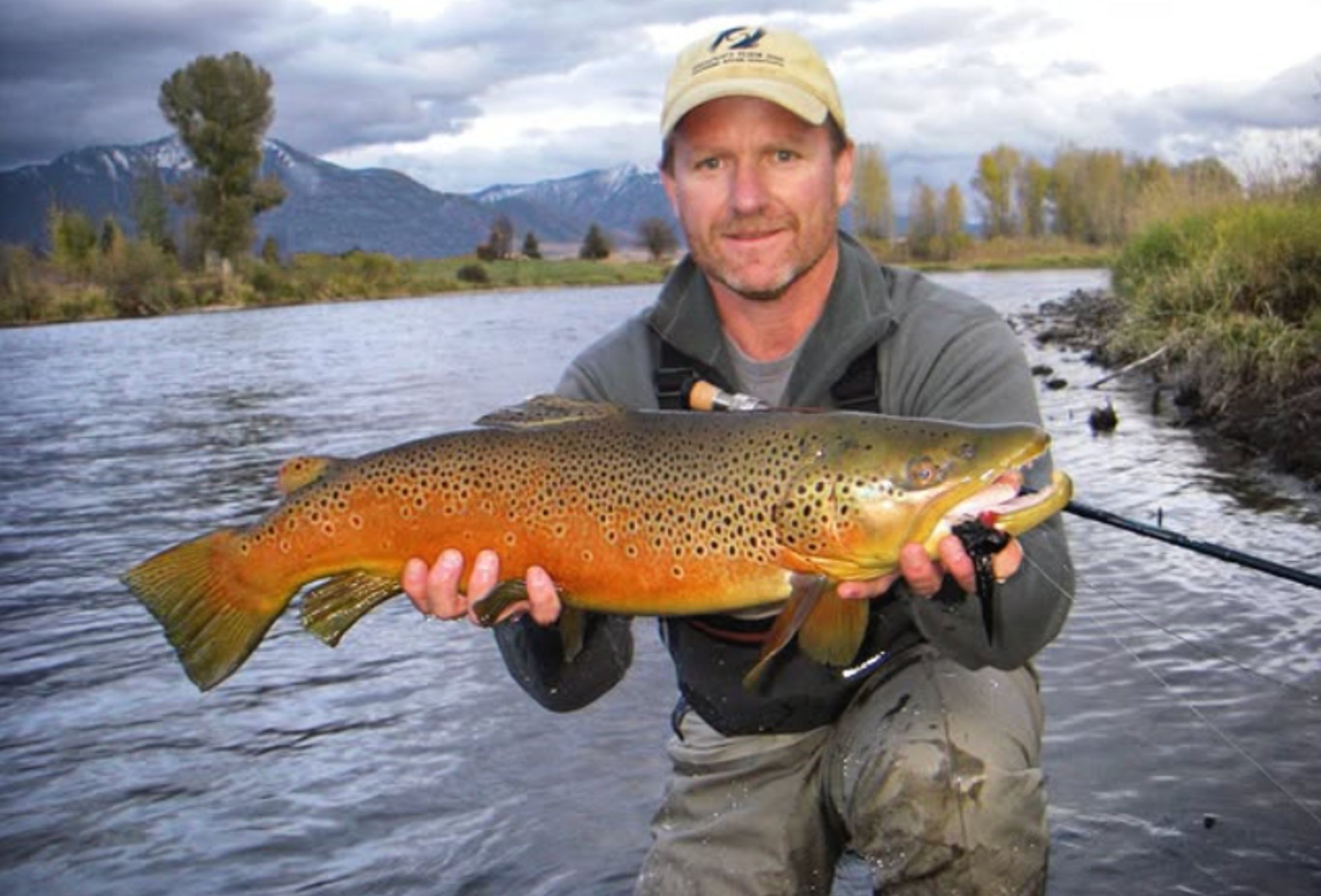 a man holds a large brown trout on a river