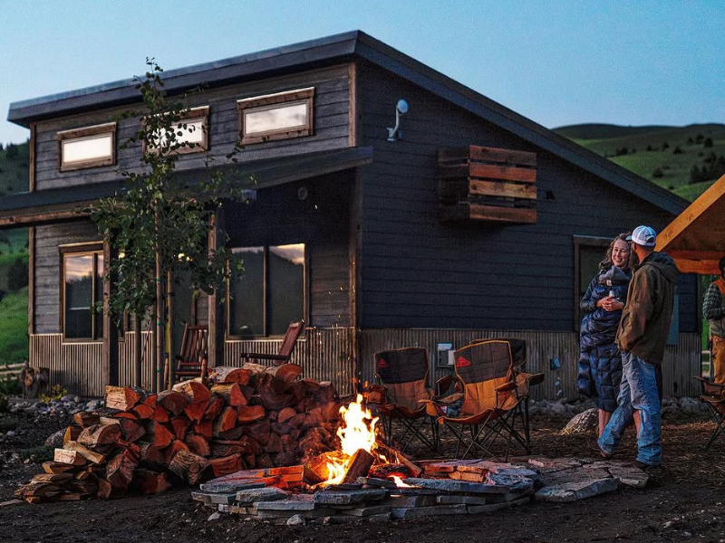 two people by a campfire with a rock creek cabin 