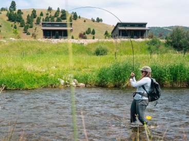 a woman stands in a stream while fly fishing