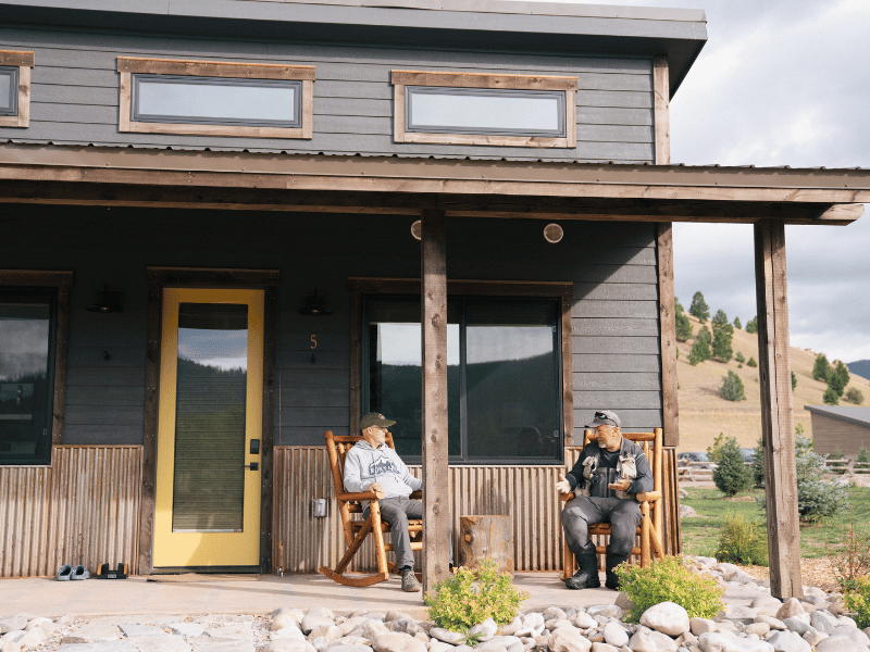 two men sit in rocking chairs in front of a cabin