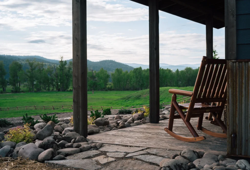 a rocking chair on the porch of a cabin overlooking a green field