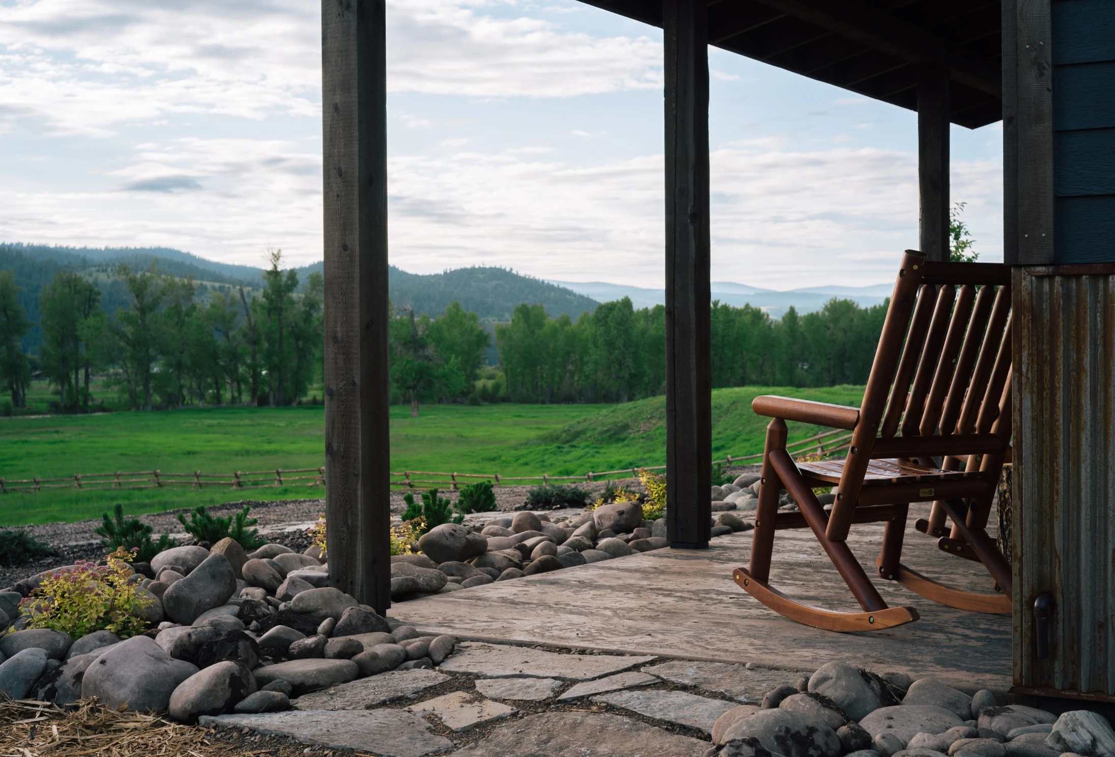 a rocking chair on the porch of a cabin overlooking a green field