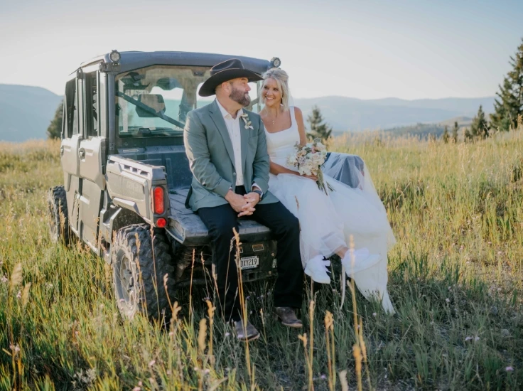 a bride and groom sit on the back of a side by side
