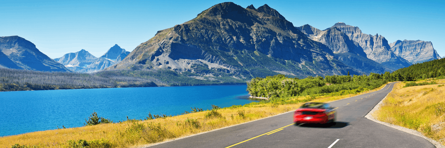 a red sports car driving along an alpine lake in glacier national park