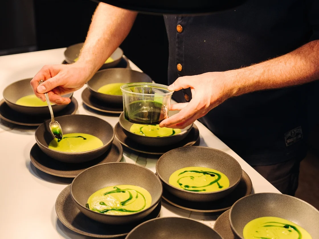 a chef adding green condiment to a number of bowls of soup