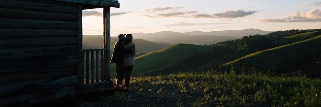 two people hold each other while overlooking a sunset in the mountains of montana