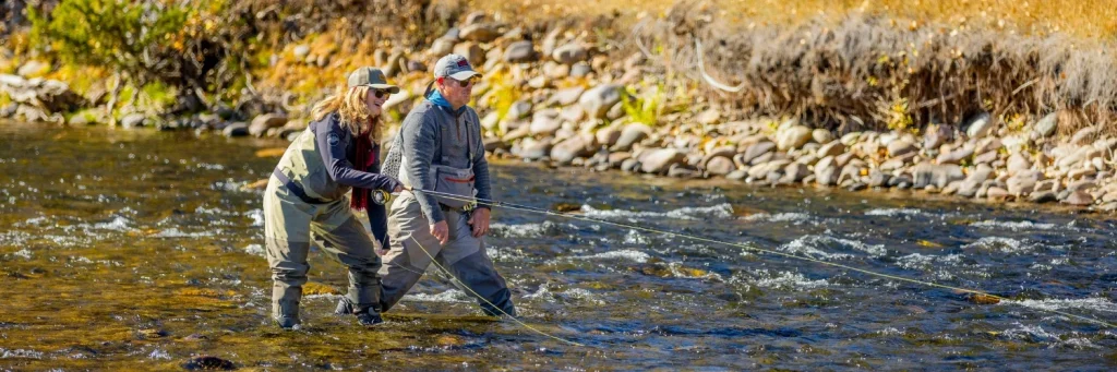 two people stand in a river while fly fishing